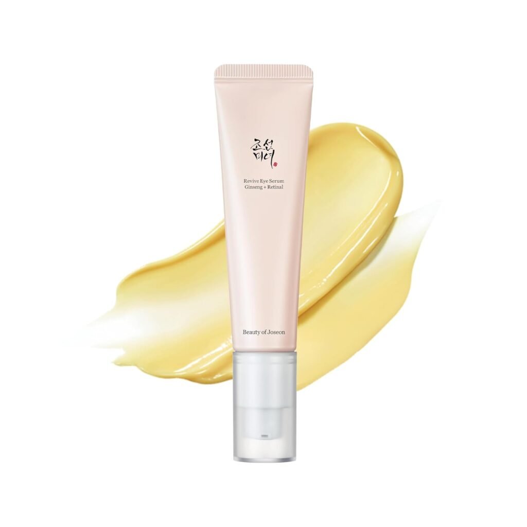 A pink tube of eye serum with Korean text stands upright in front of a creamy yellow smear, against a white background. The label reads Beauty of Joseon Revive Eye Serum, formulated to target under eye circles causes.